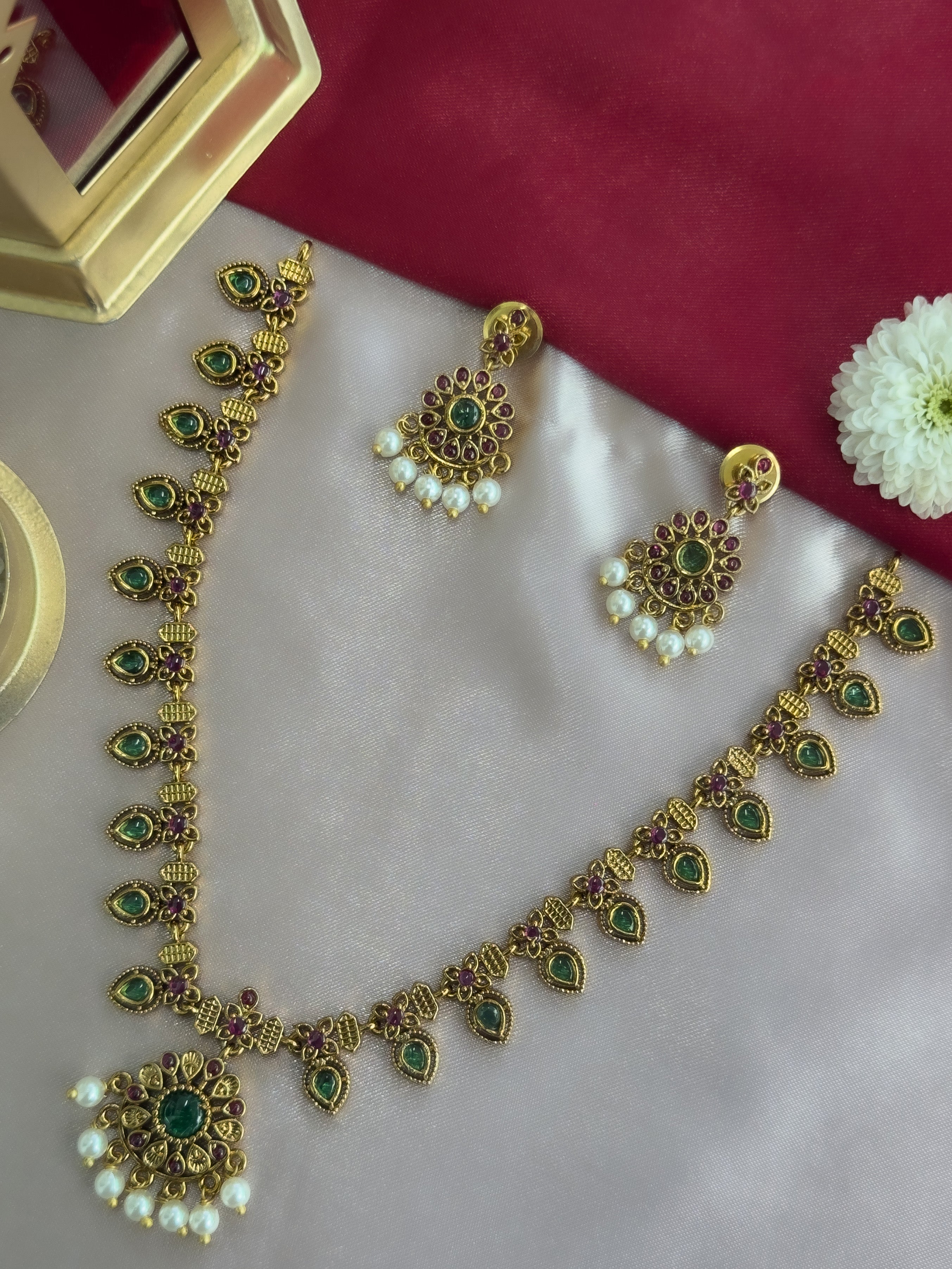Gold palakka mala necklace with green gemstones and matching earrings on a white surface.