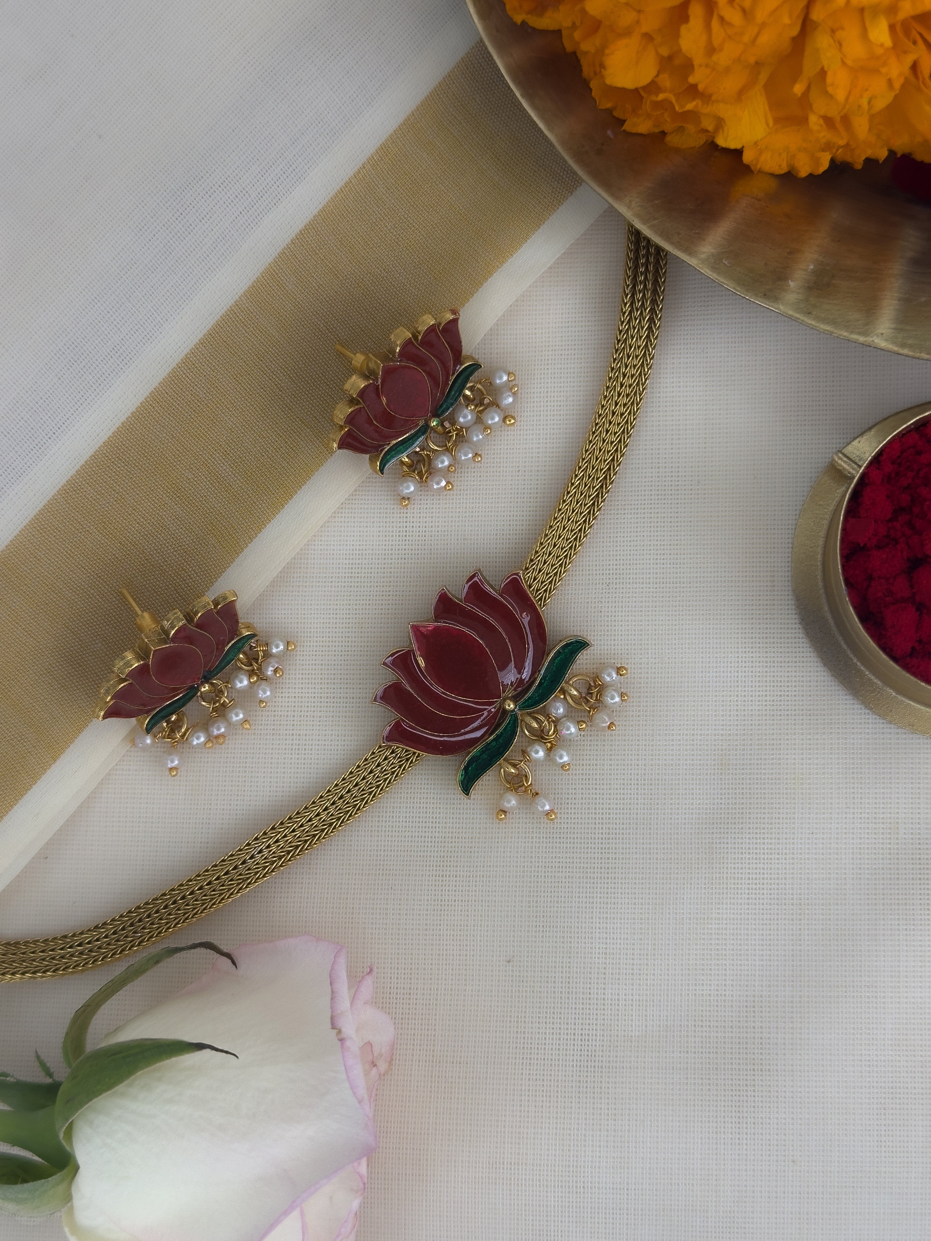 Ethnic choker with Lotus designs with matching earrings on a white surface with flowers and a tray in the background.