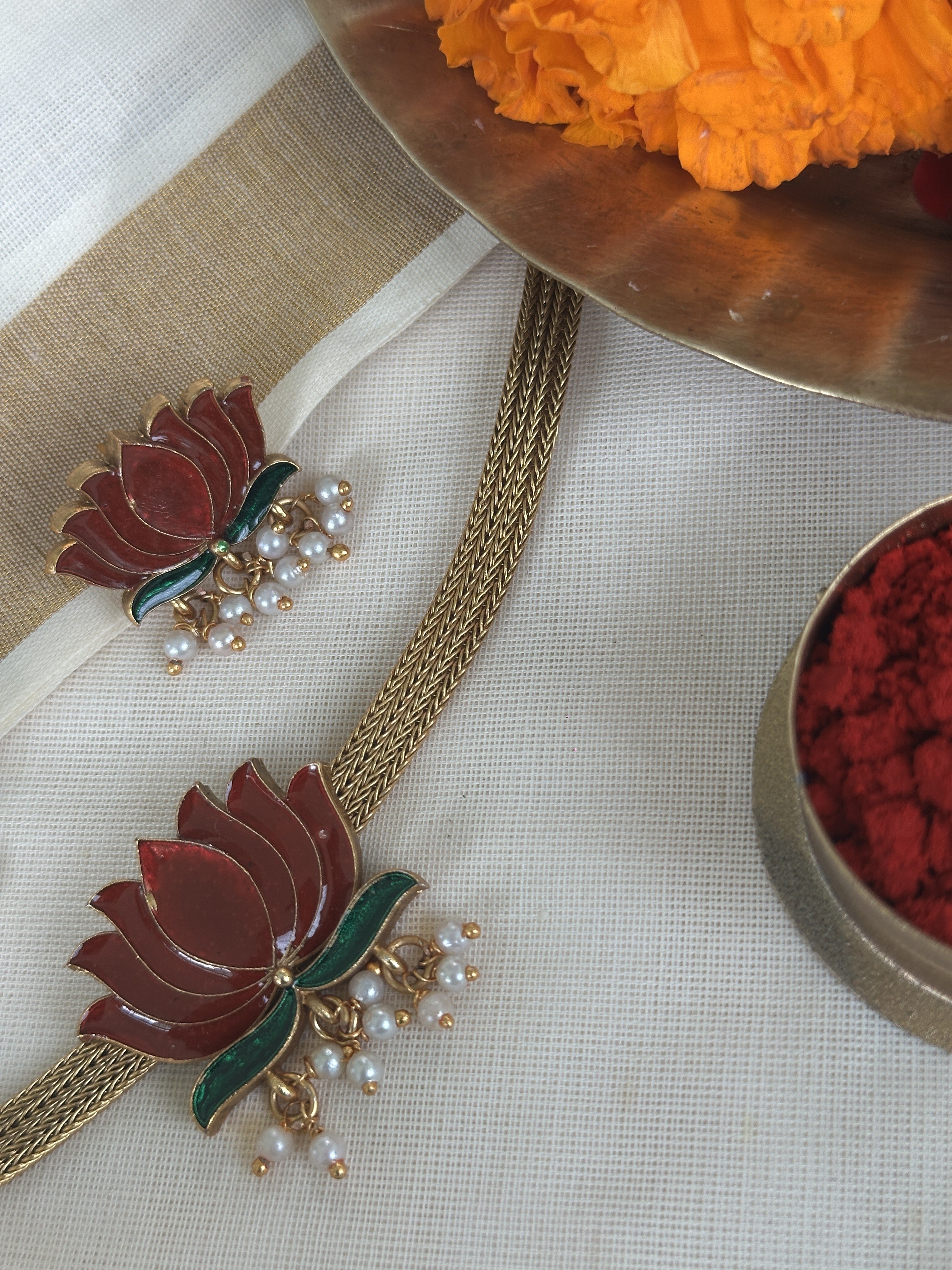 Ethnic choker with Lotus designs with matching earrings on a white surface with flowers and a tray in the background.