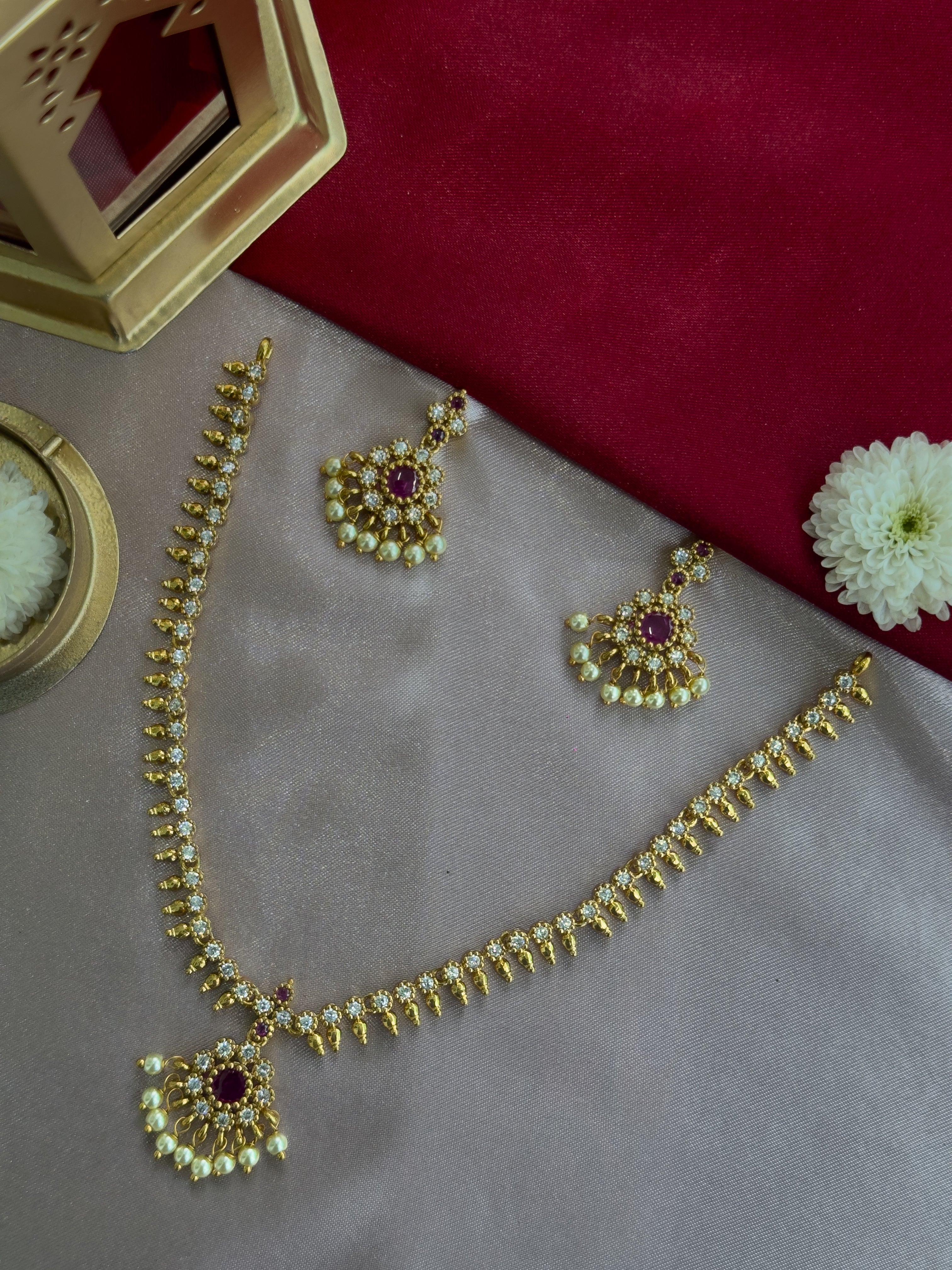Ethnic Gold kemp attige necklace with red stones and AD stones  on a gray surface with a red fabric background