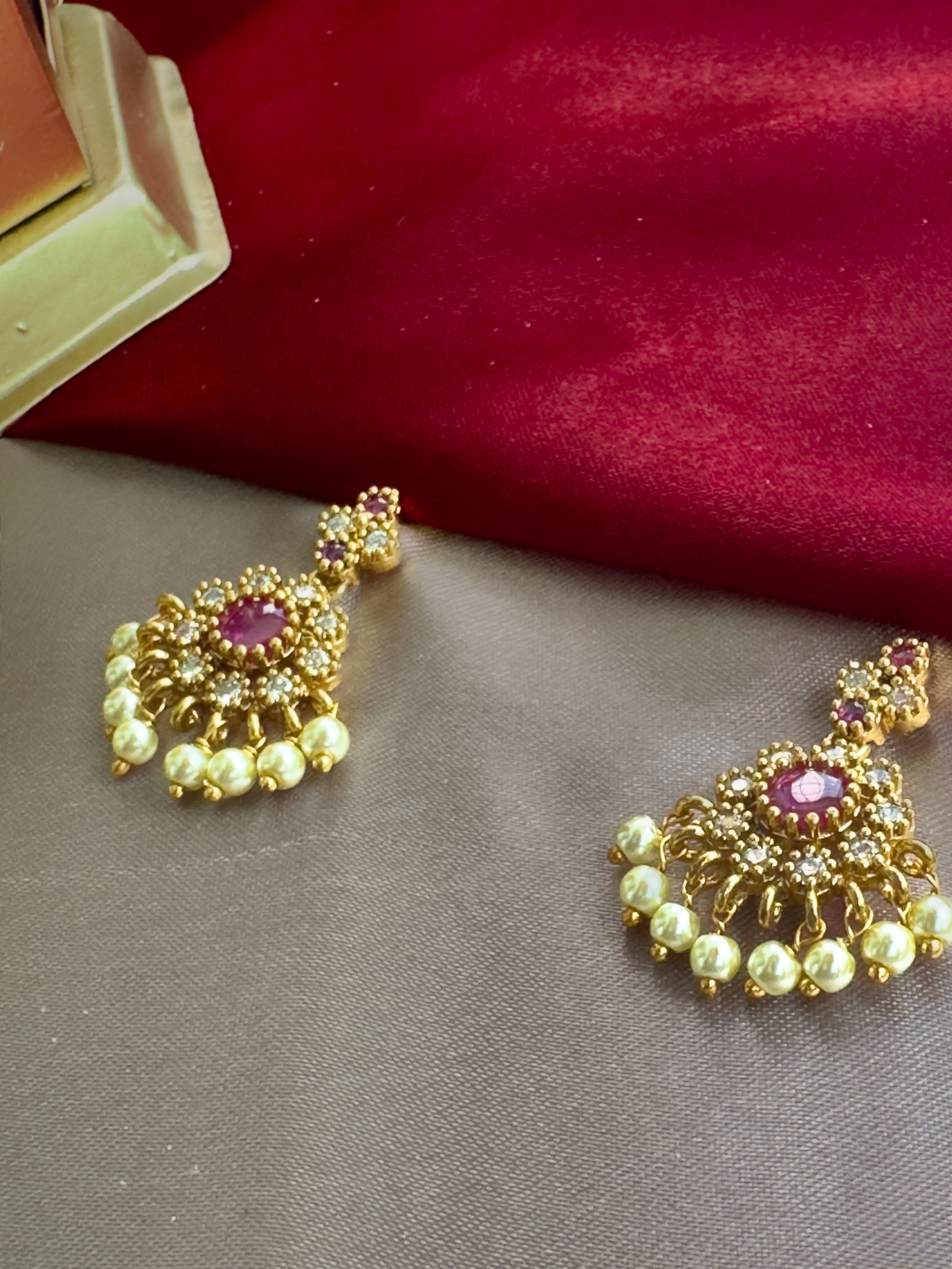 Ethnic Gold kemp attige necklace with red stones and AD stones  on a gray surface with a red fabric background