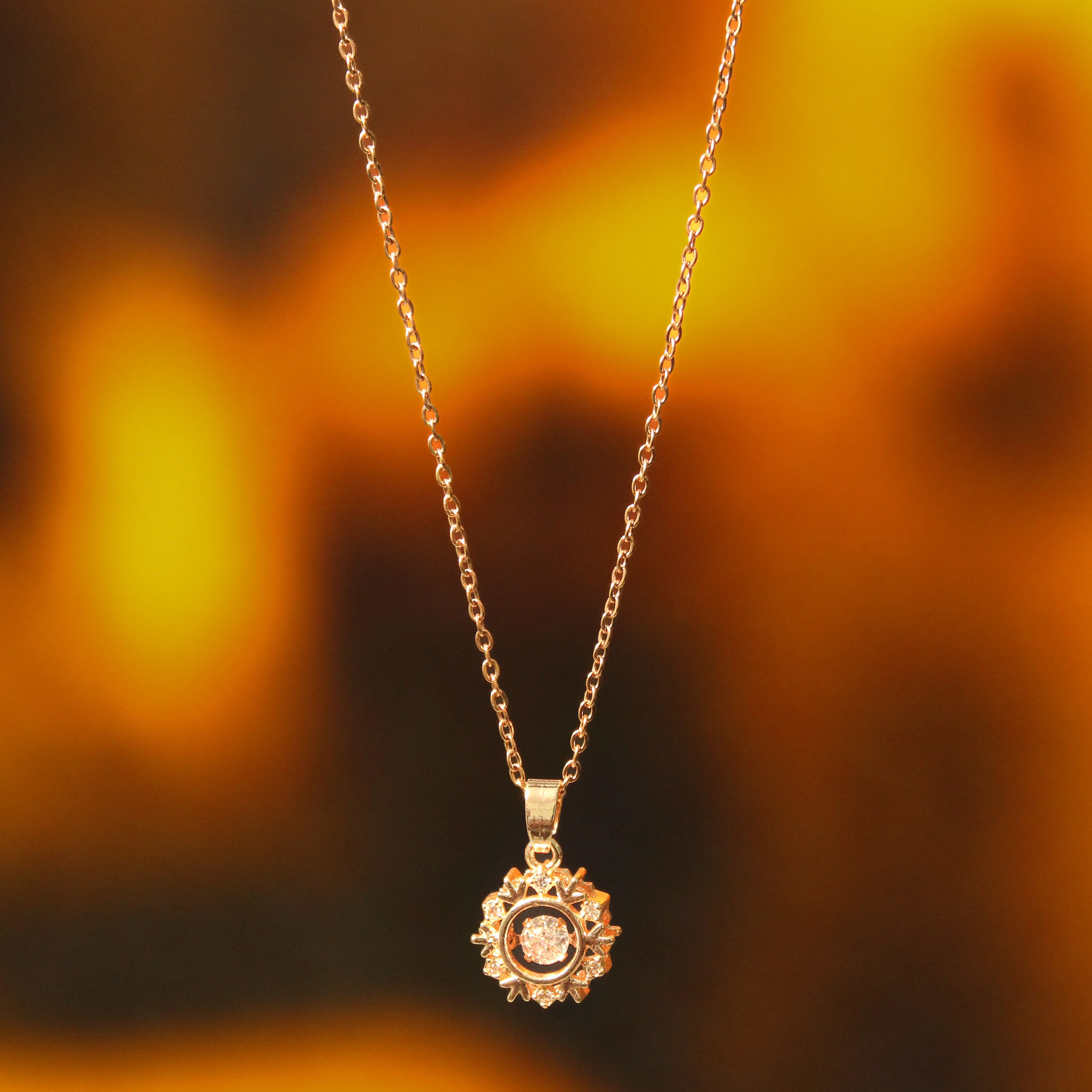 Gold necklace with a sunflower pendant against a blurred autumn background