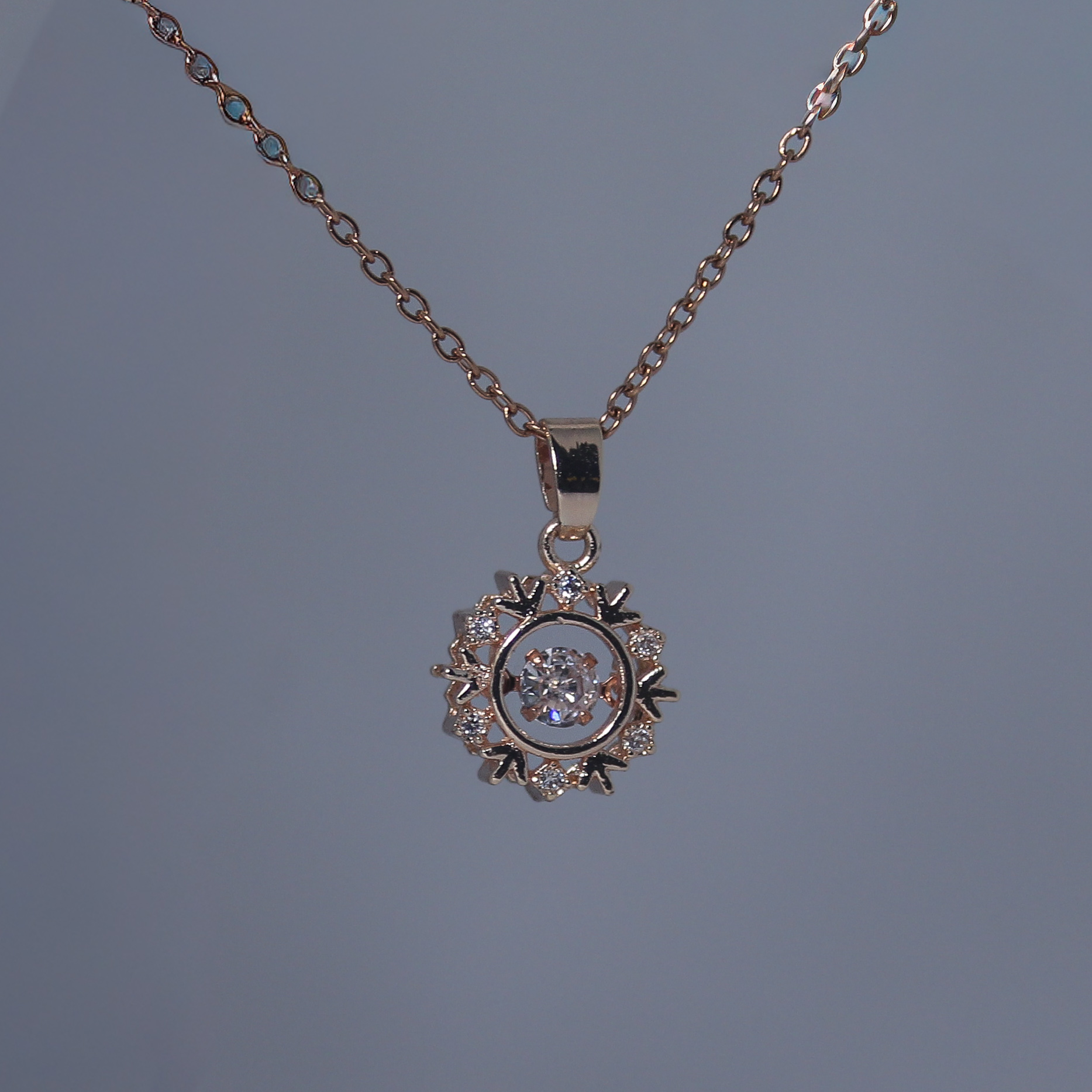 Rose gold necklace with a round pendant on a gray background