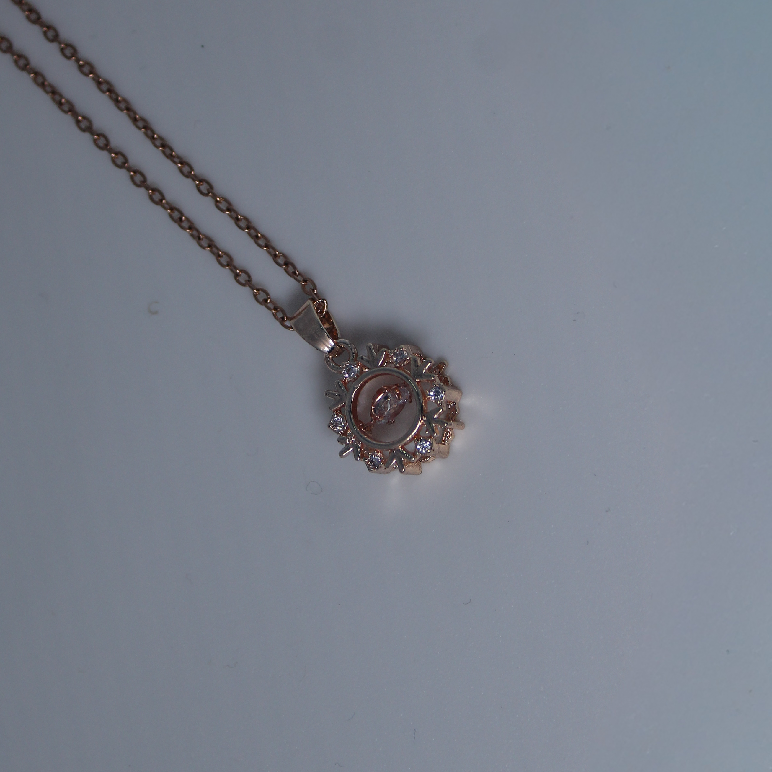 Rose gold anti tarnish necklace with a circular pendant on a light gray background
