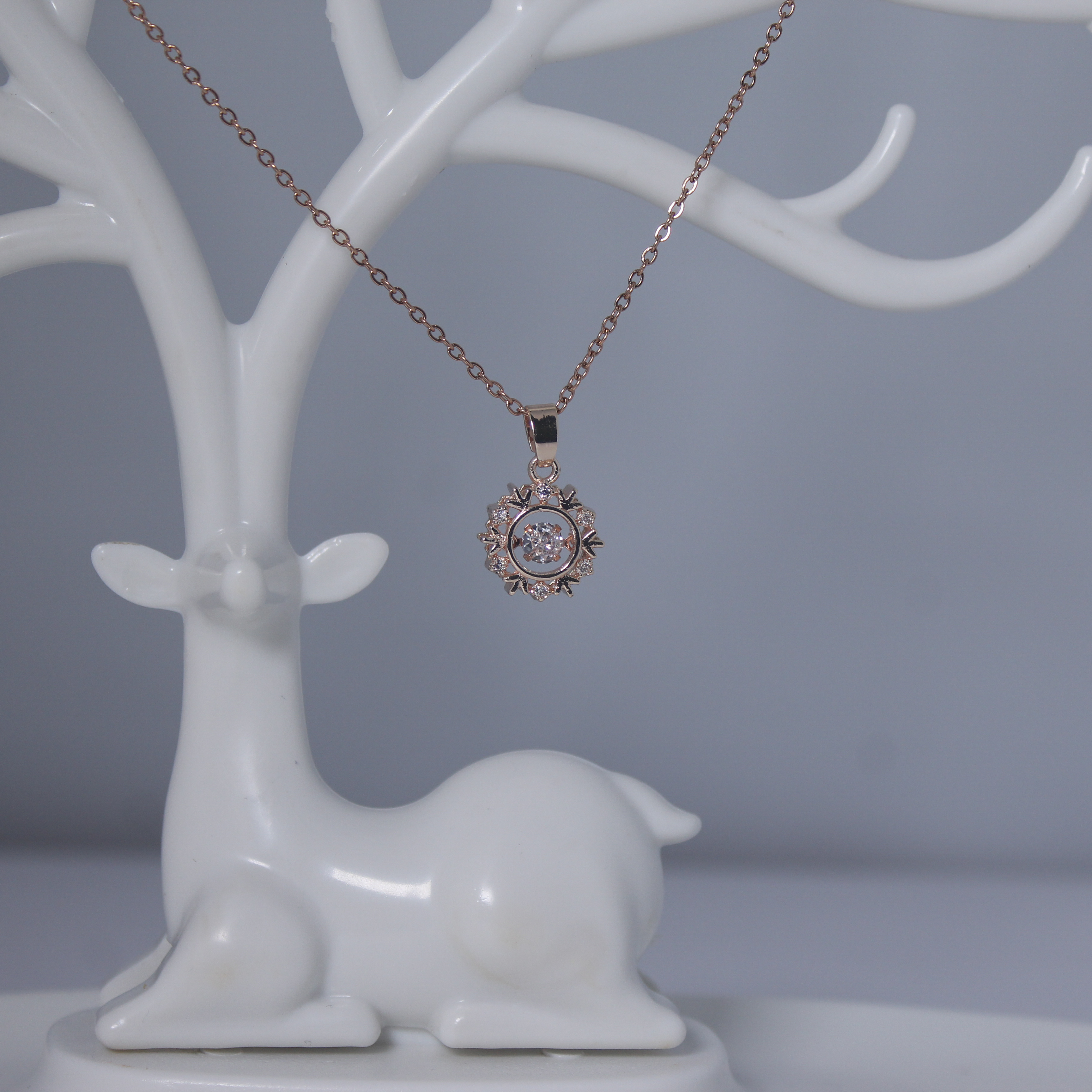 Rose gold anti tarnish necklace with a diamond pendant on a white ceramic deer stand against a gray background
