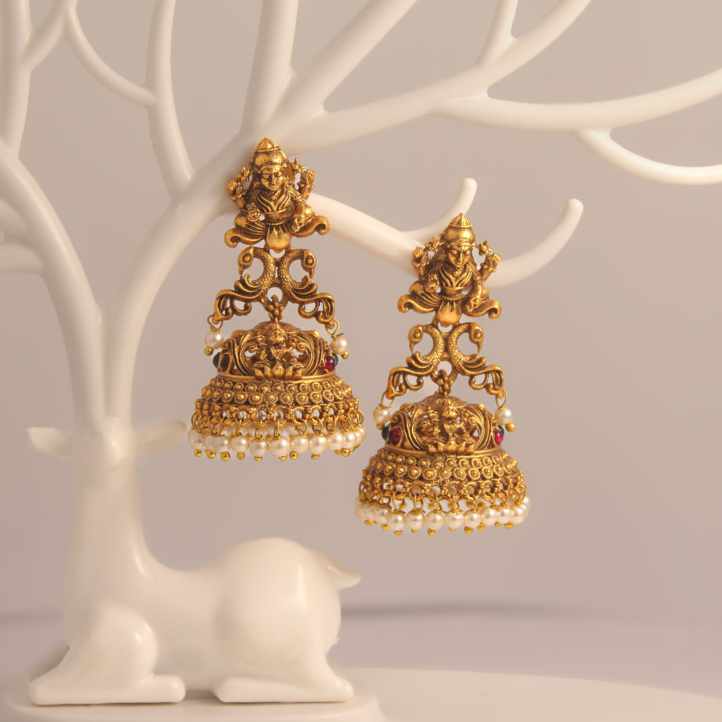 Gold ethnic earrings with intricate designs on a white tree-like stand.