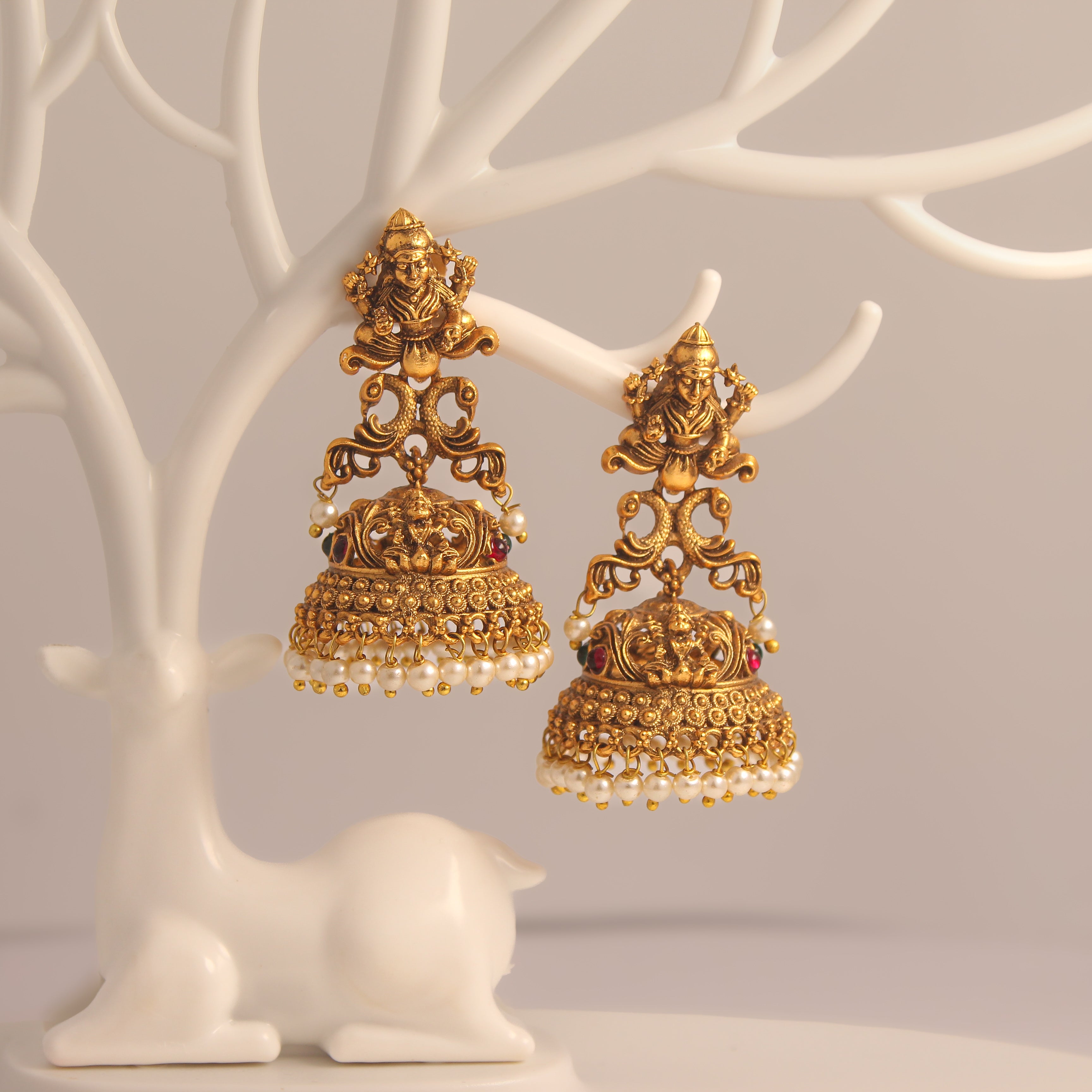 Gold ethnic earrings with intricate designs on a white tree-like stand.