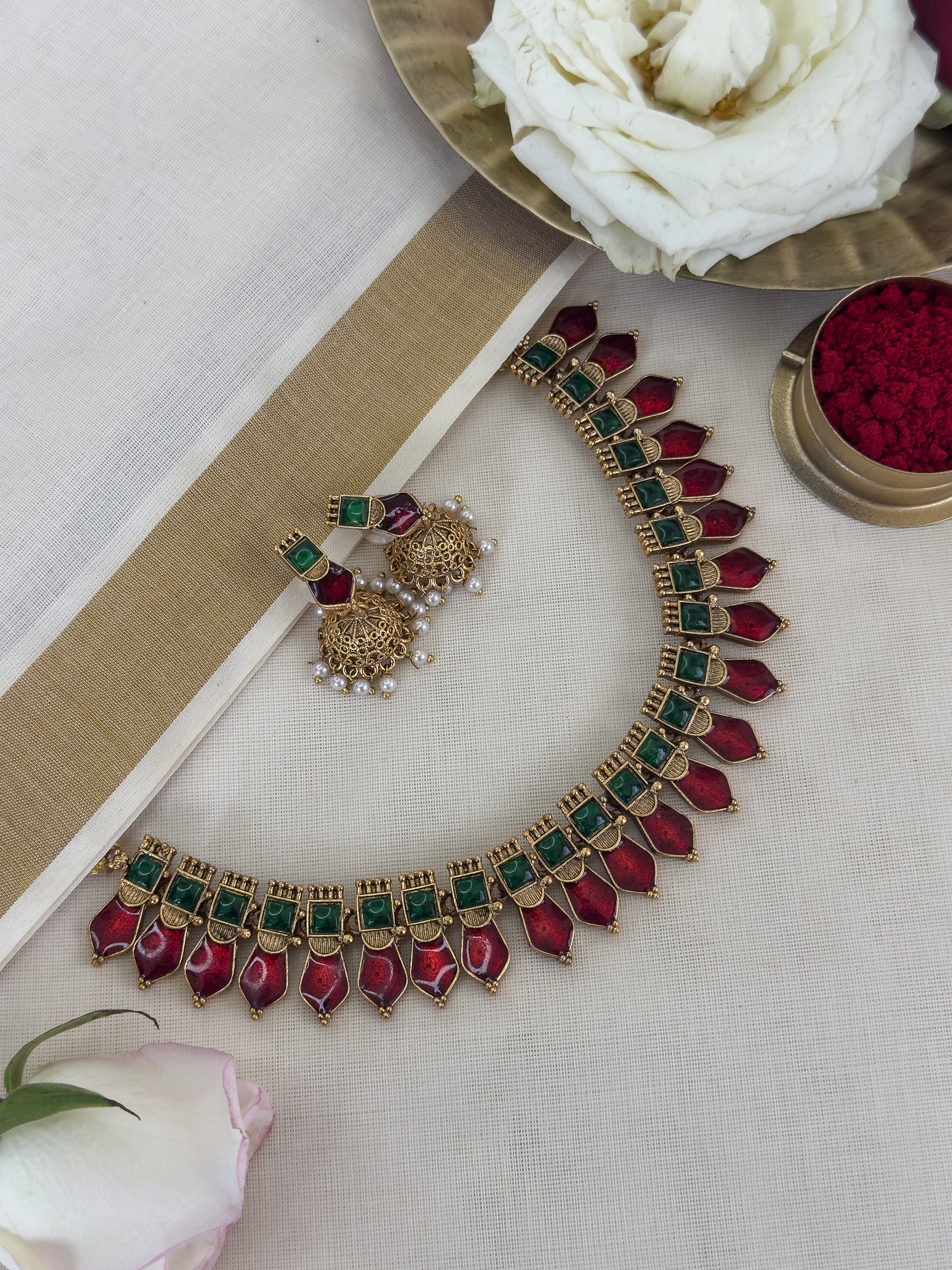 Ethnic Nagapadam necklace with red and green gemstones with matching Jhumkas on a light background