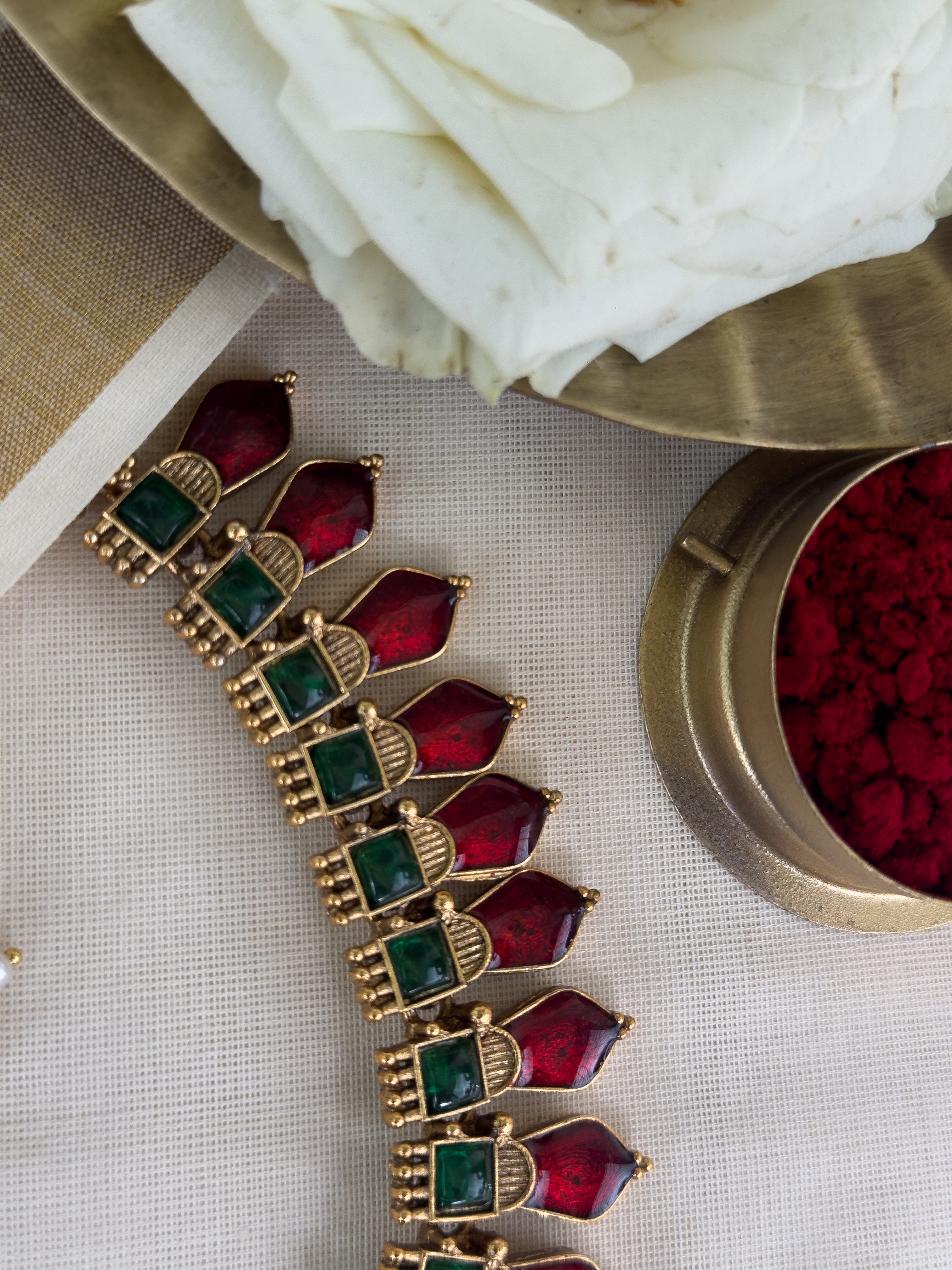 Ethnic Nagapadam necklace with red and green gemstones with matching Jhumkas on a light background
