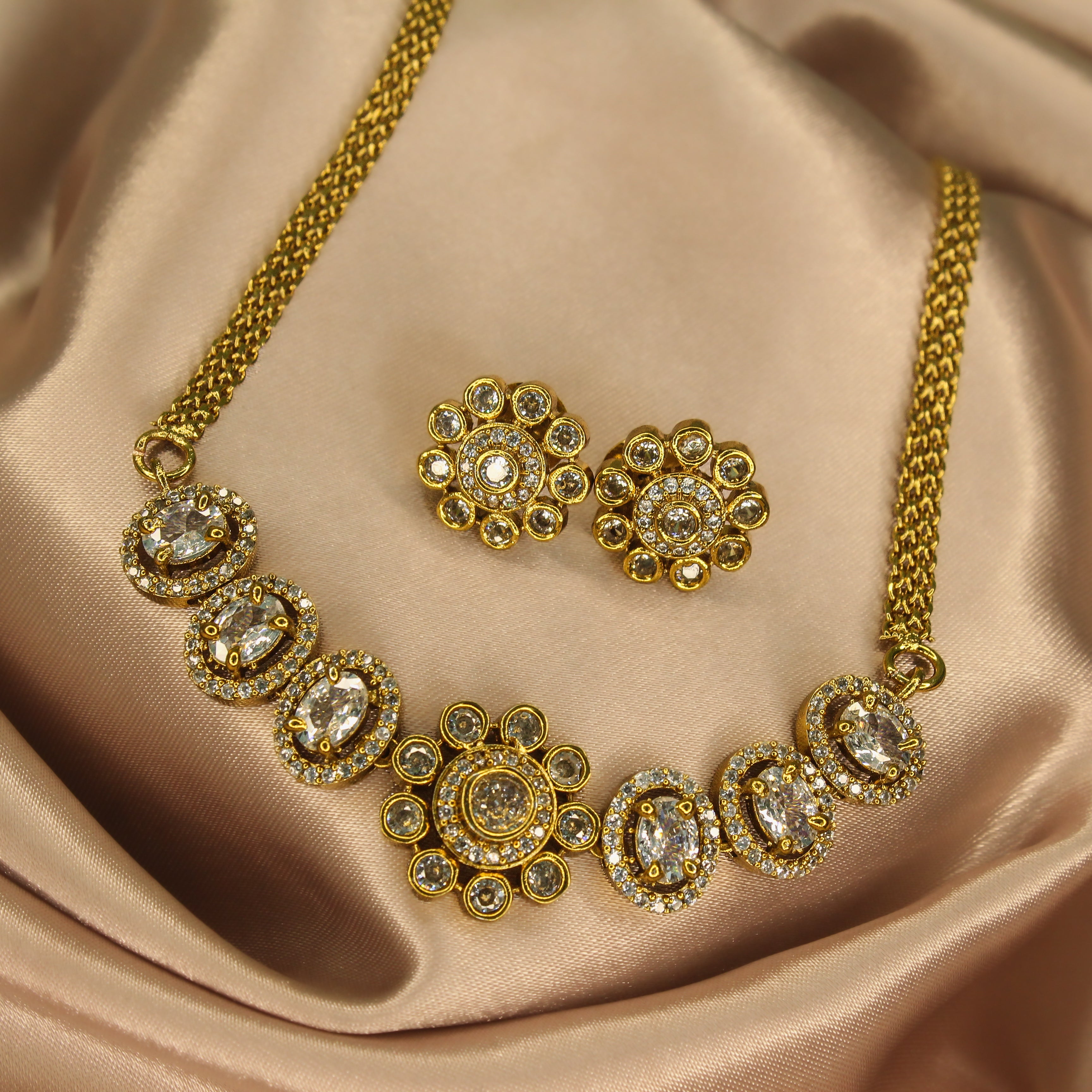 Gold AD necklace with Pastel diamond stone and matching earrings with green gemstones on a satin surface