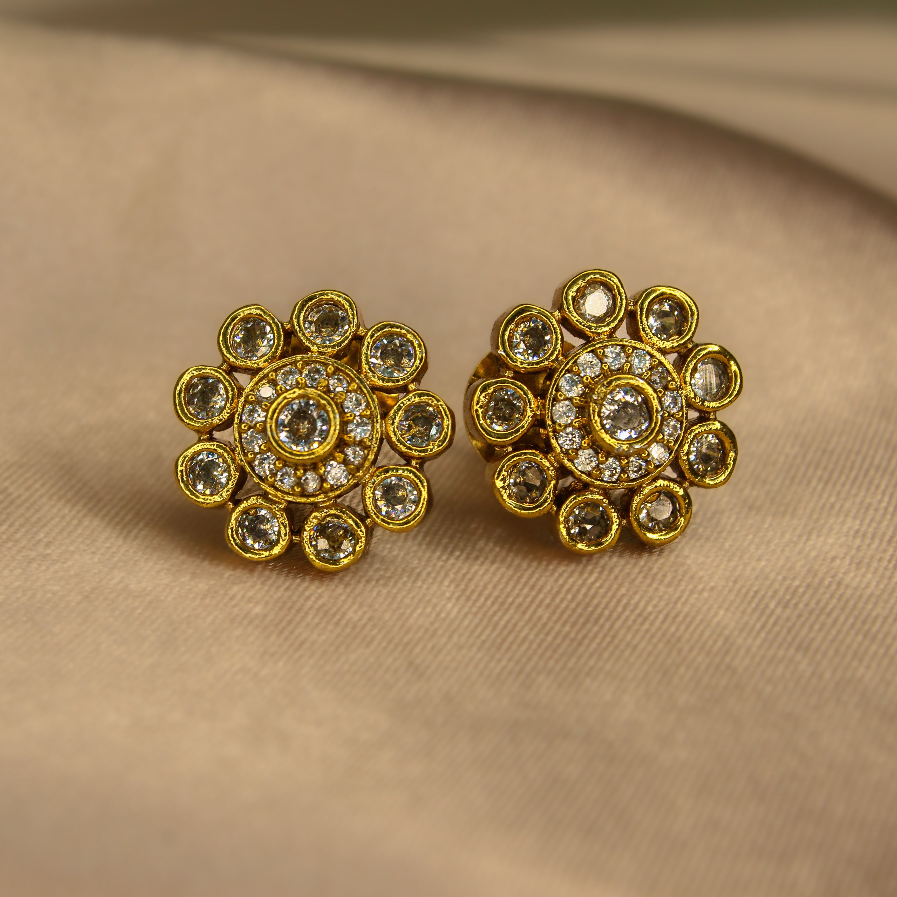 Pair of AD gold earrings with diamond gemstones on a beige fabric background