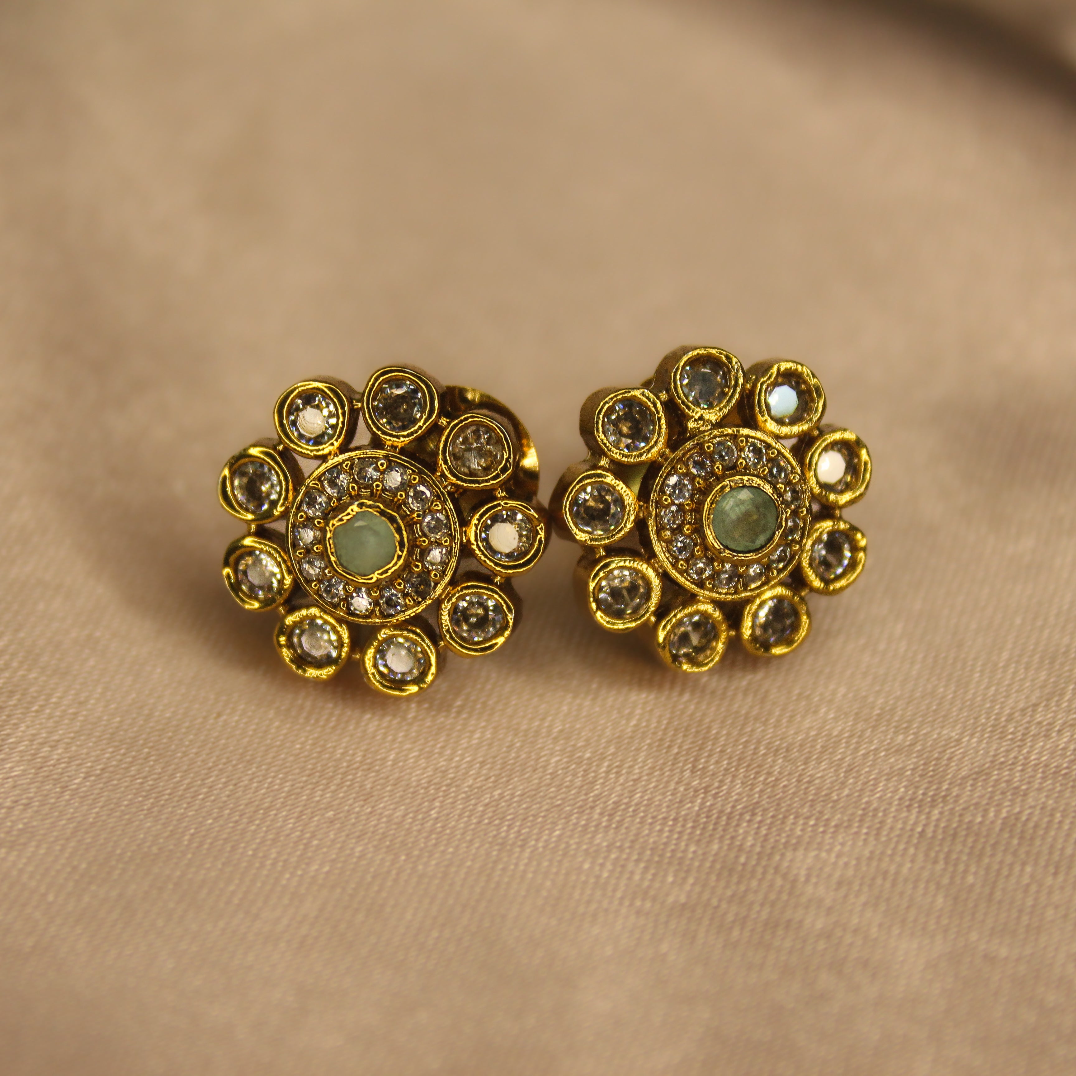 Pair of AD gold earrings with green gemstones on a beige fabric background