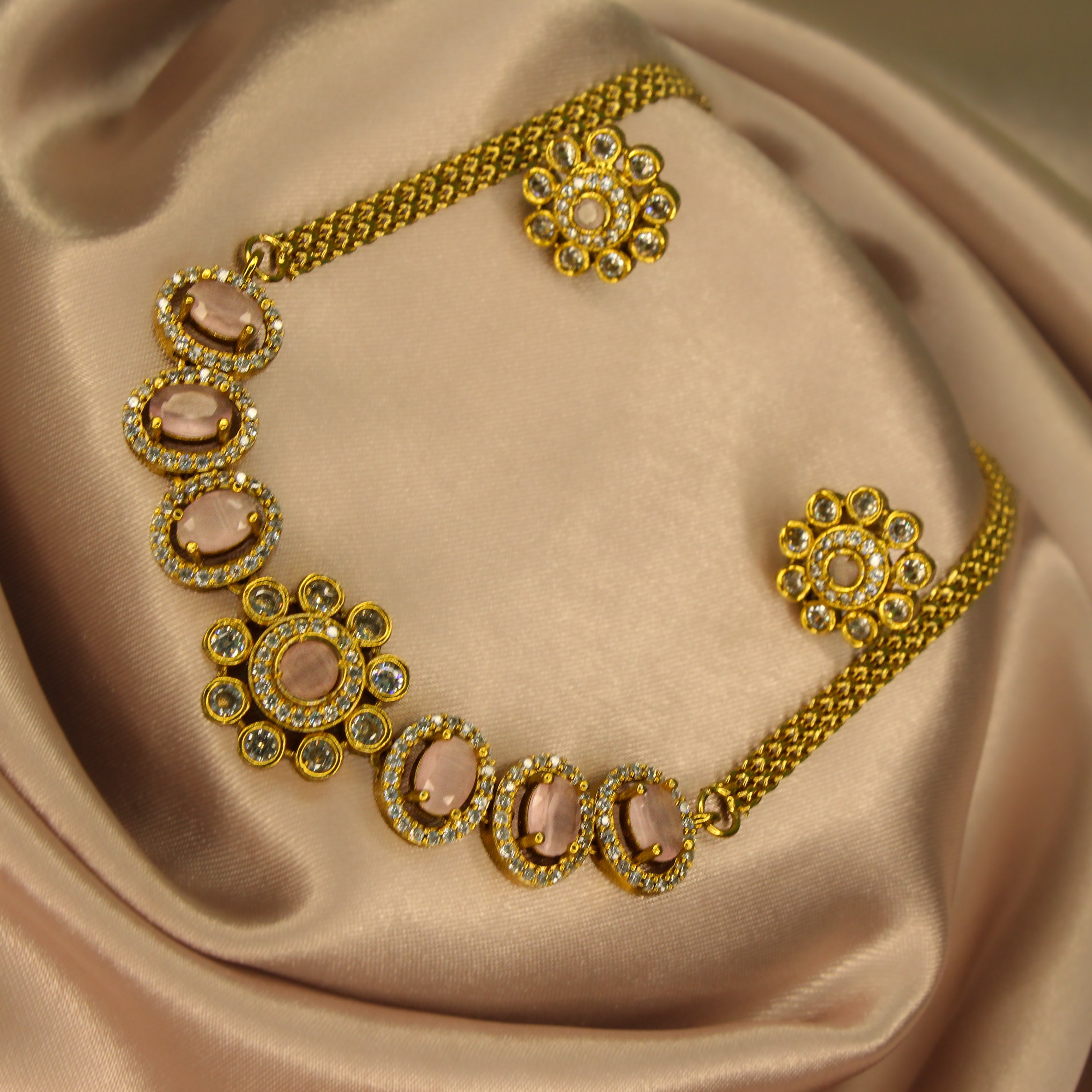 Gold AD necklace with Pastel pink and diamond stone and matching earrings with green gemstones on a satin surface