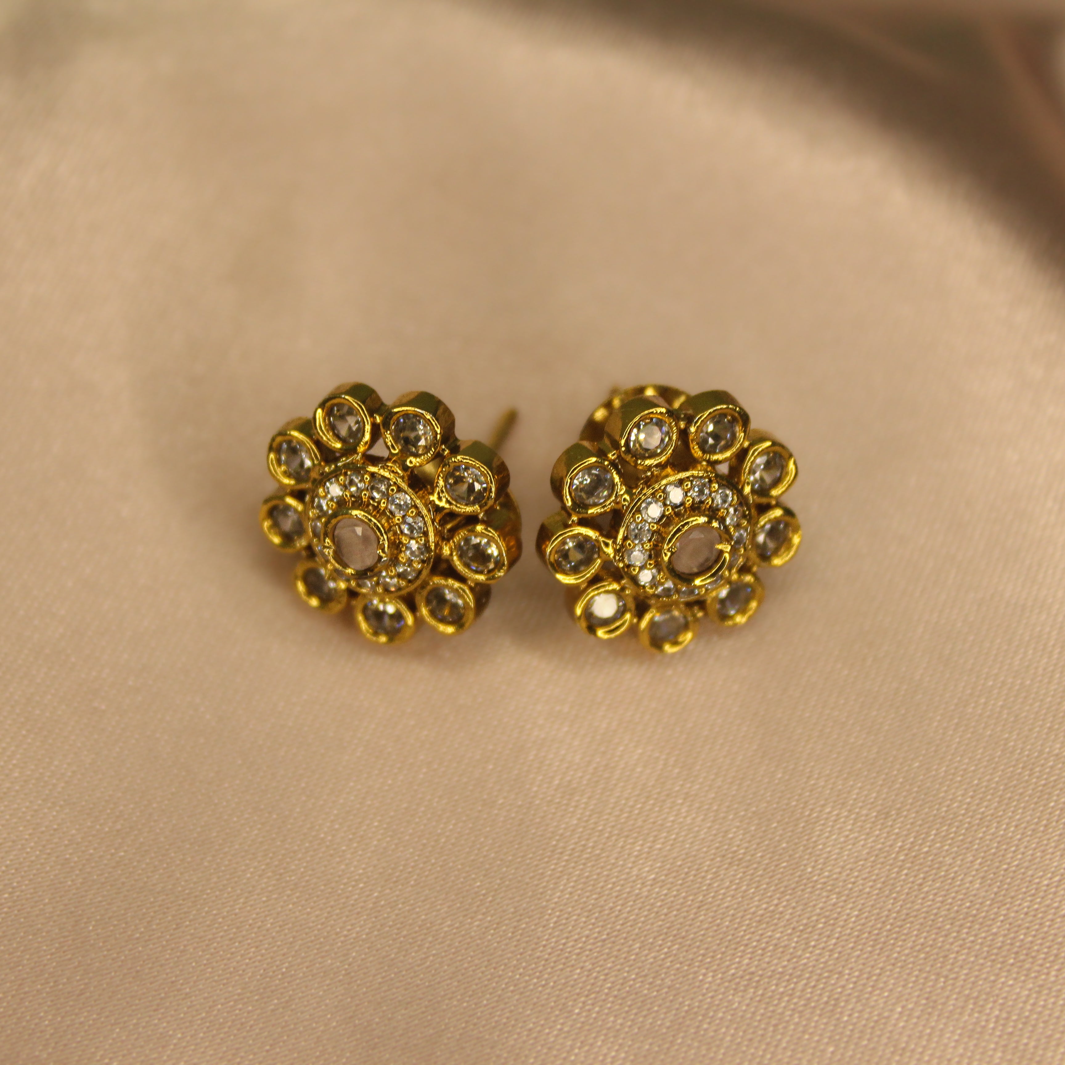 Pair of AD gold earrings with pink gemstones on a beige fabric background